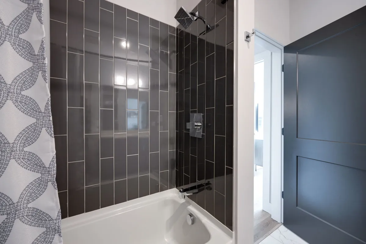 A contemporary bathroom featuring a bathtub, showerhead, sleek tile wall, and a simple shower curtain. The design is modern and peaceful, ideal for both quick showers and long, leisurely baths.