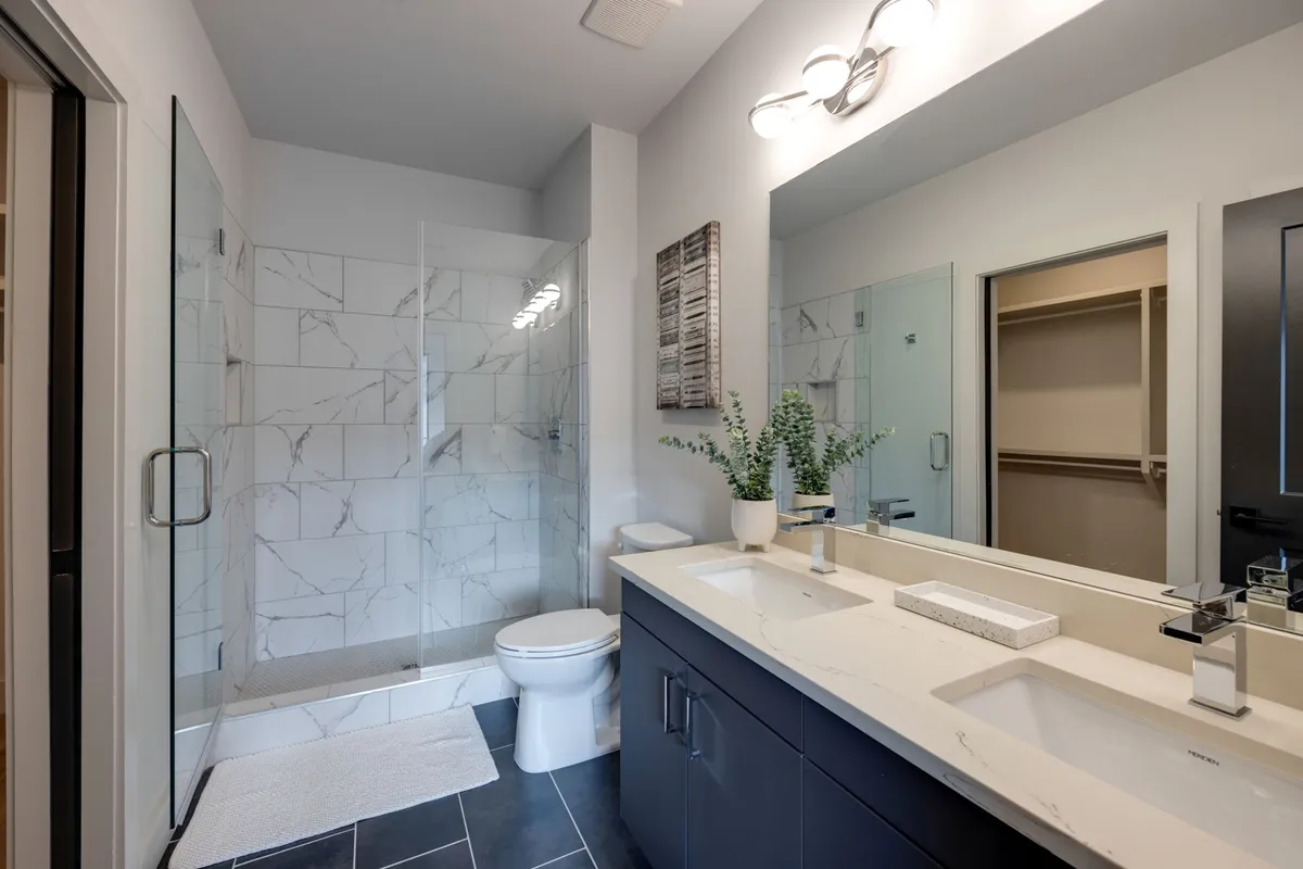 A spa-inspired bathroom featuring a double sink vanity, glass shower enclosure, textured wall art, and a touch of greenery. The space is bright, modern, and exudes luxury, inviting relaxation and self-care.