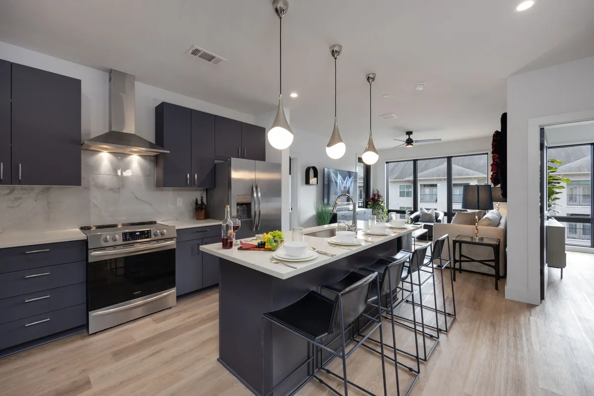 The image features a stylish kitchen with a central island, stainless steel appliances, pendant lighting, and a welcoming dining setup. The ambiance is modern yet cozy, perfect for both cooking and social gatherings.